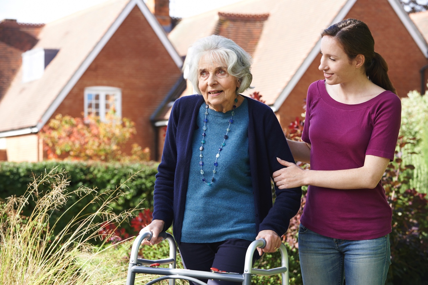 A young woman helping a senior woman with a walker in the garden