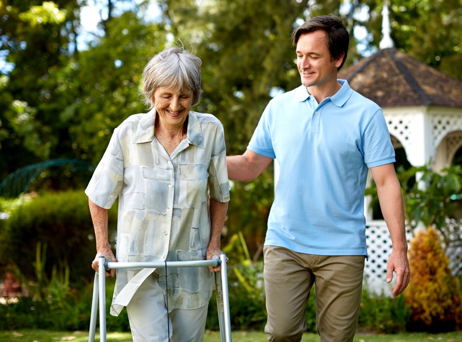 A male staff member helping a senior woman with a walker in the garden