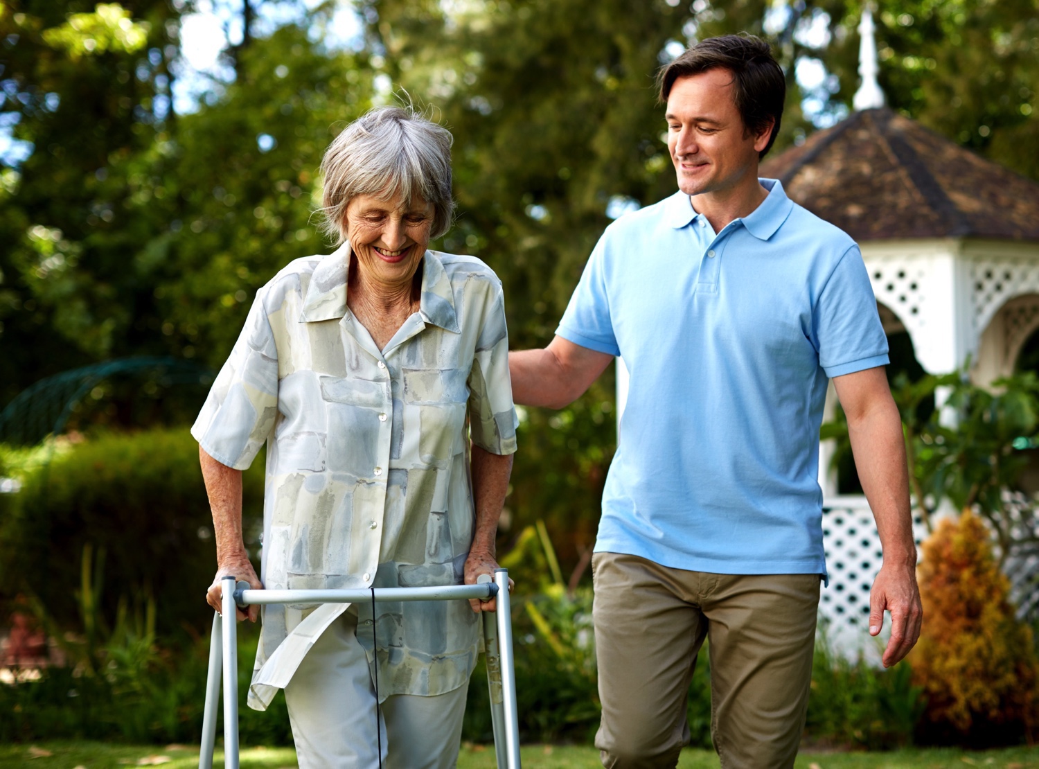 A male staff member helping a senior woman with a walker in the garden