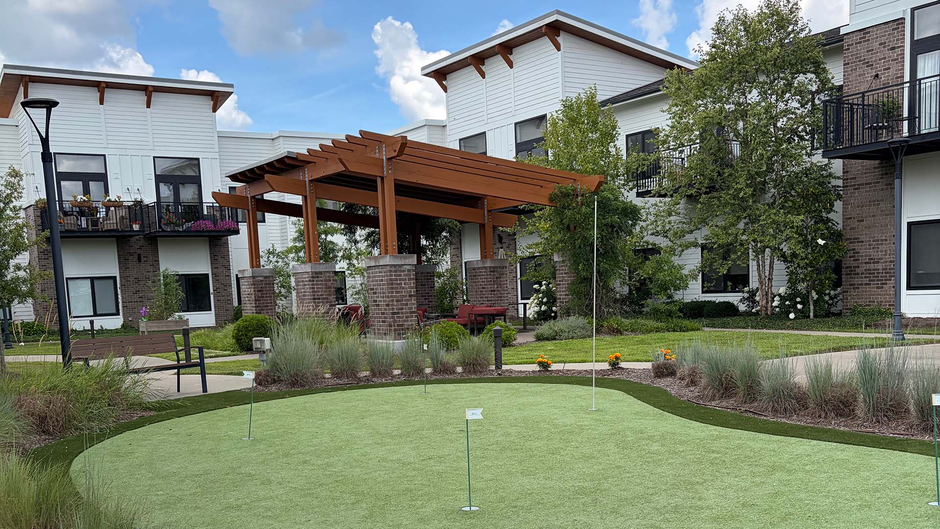 The outdoor putting green at Cedarhurst of Hamburg featuring an adjacent shaded pergola and modern, comfortable seating for residents.