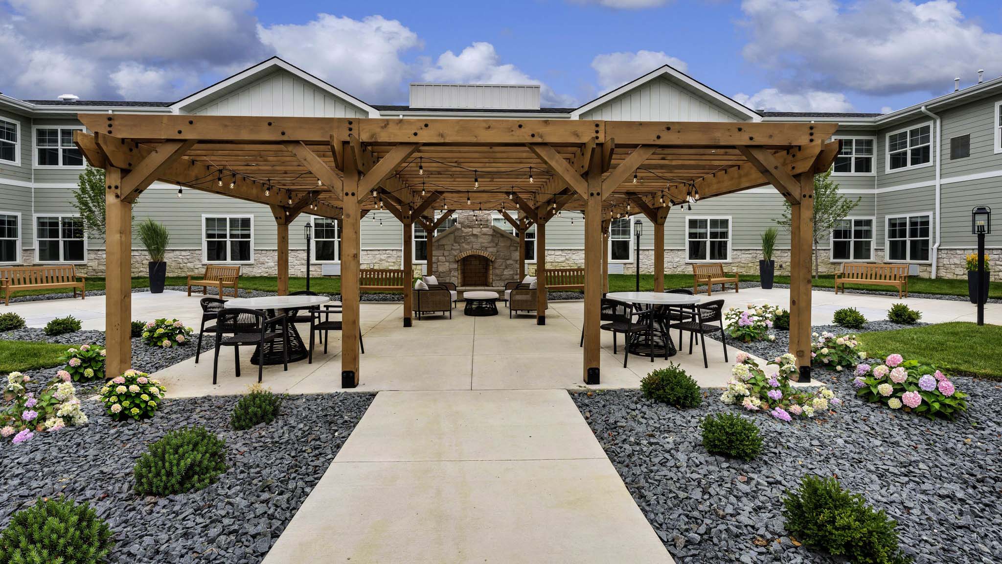 Outdoor green space at Cedarhurst of Lincoln with paved walking paths, a wooden pergola, and fireplace