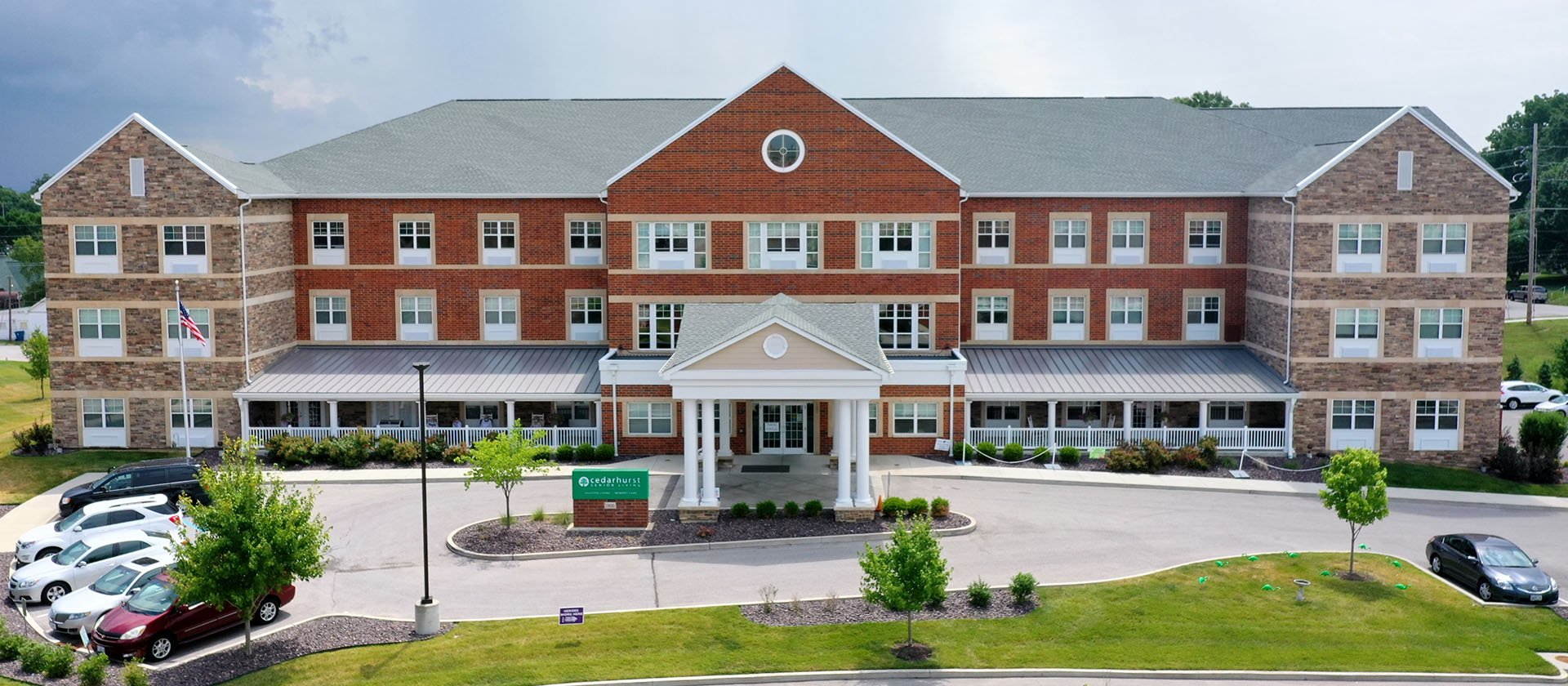 An inviting view of the Cedarhurst of St. Charles senior living community from the outside, complete with the main building and its distinctive sign