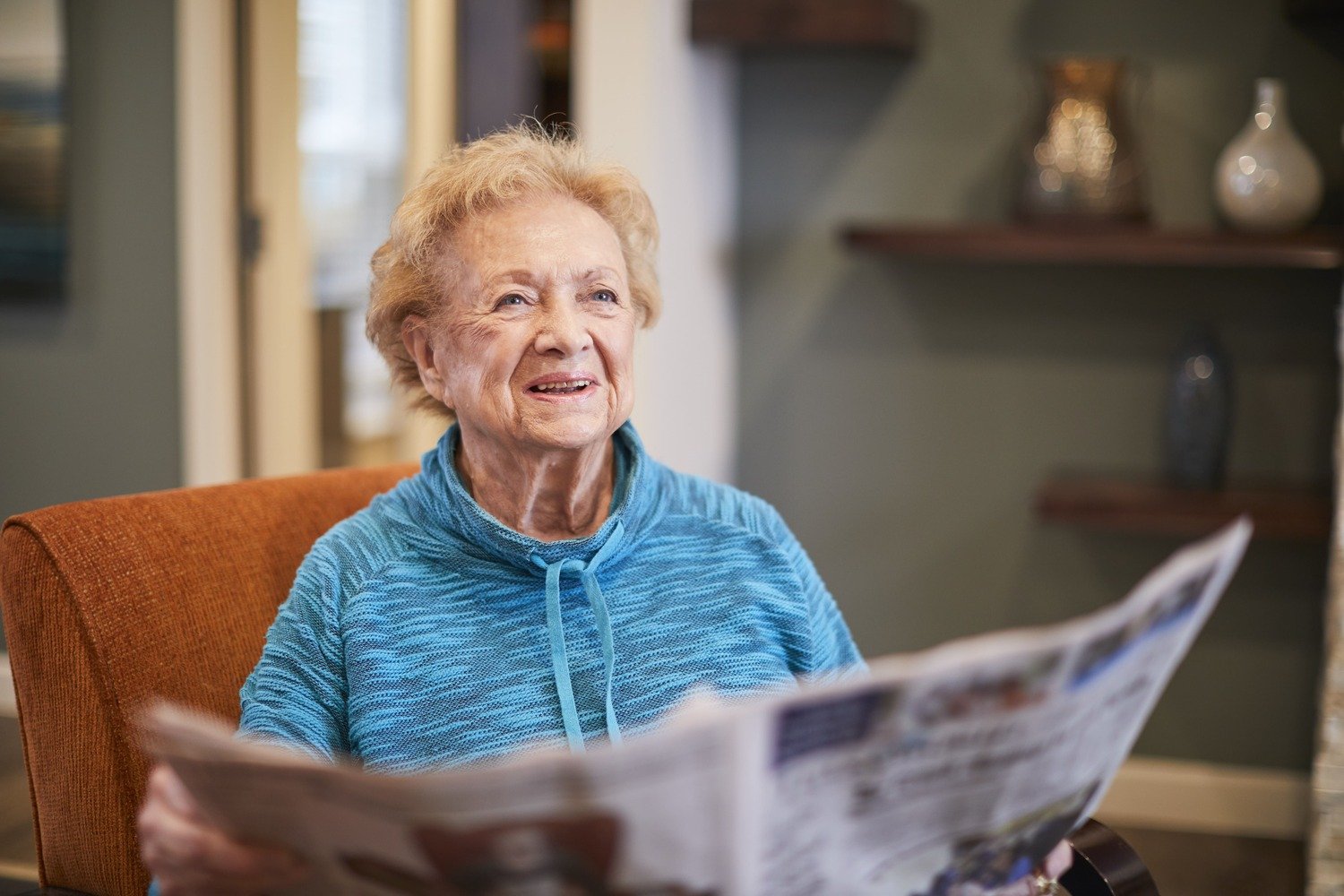 senior woman sitting in chair while reading newspaper