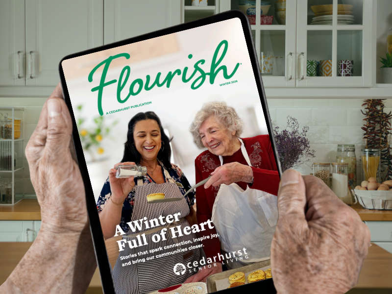 An older adult holds a tablet with an issue of Flourish magazine on the screen. The title of the issue reads 'A Winter Full of Heart,' and the cover depicts a senior living resident and a community staff member baking together.
