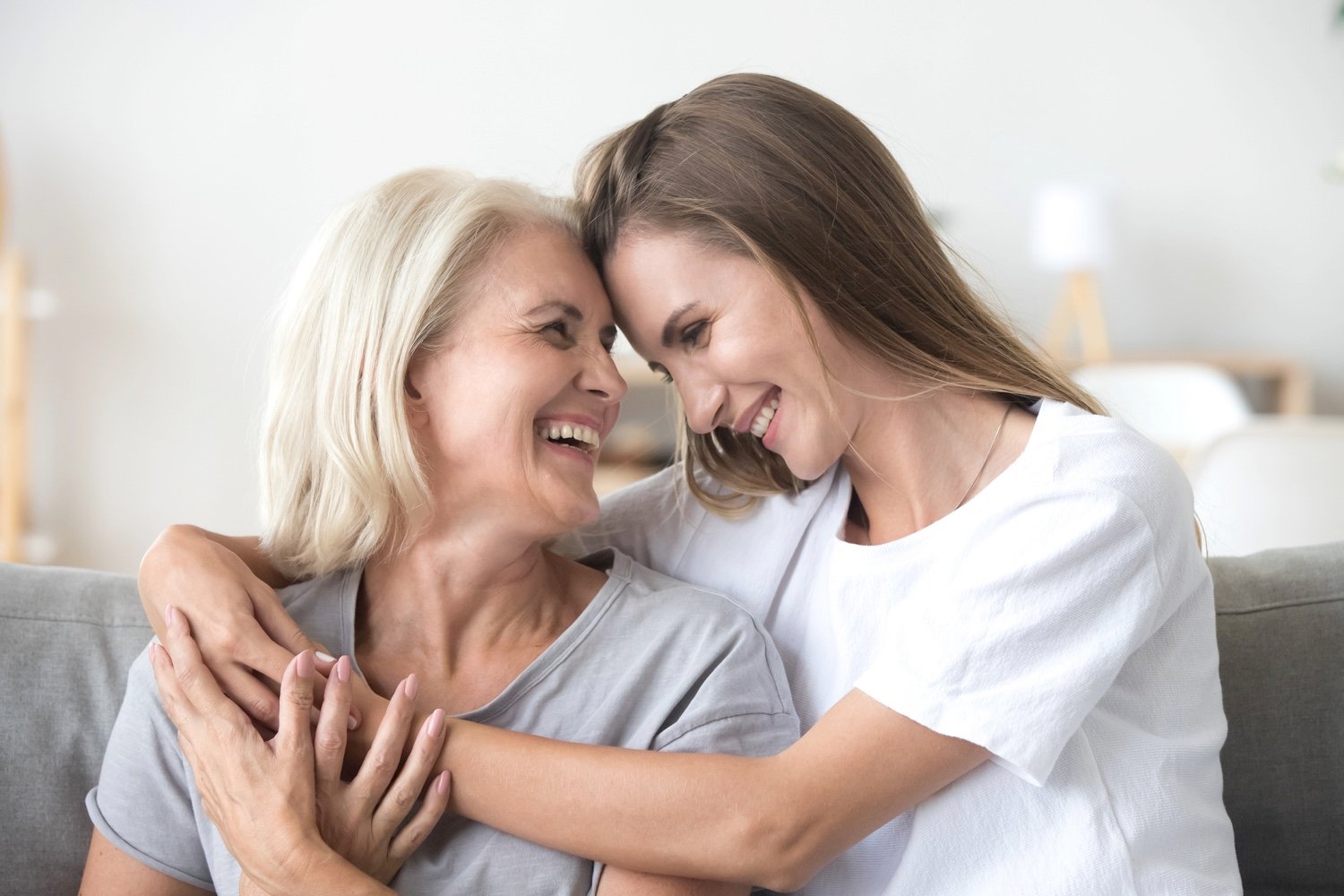 A senior woman and her daughter smiling and embracing each other