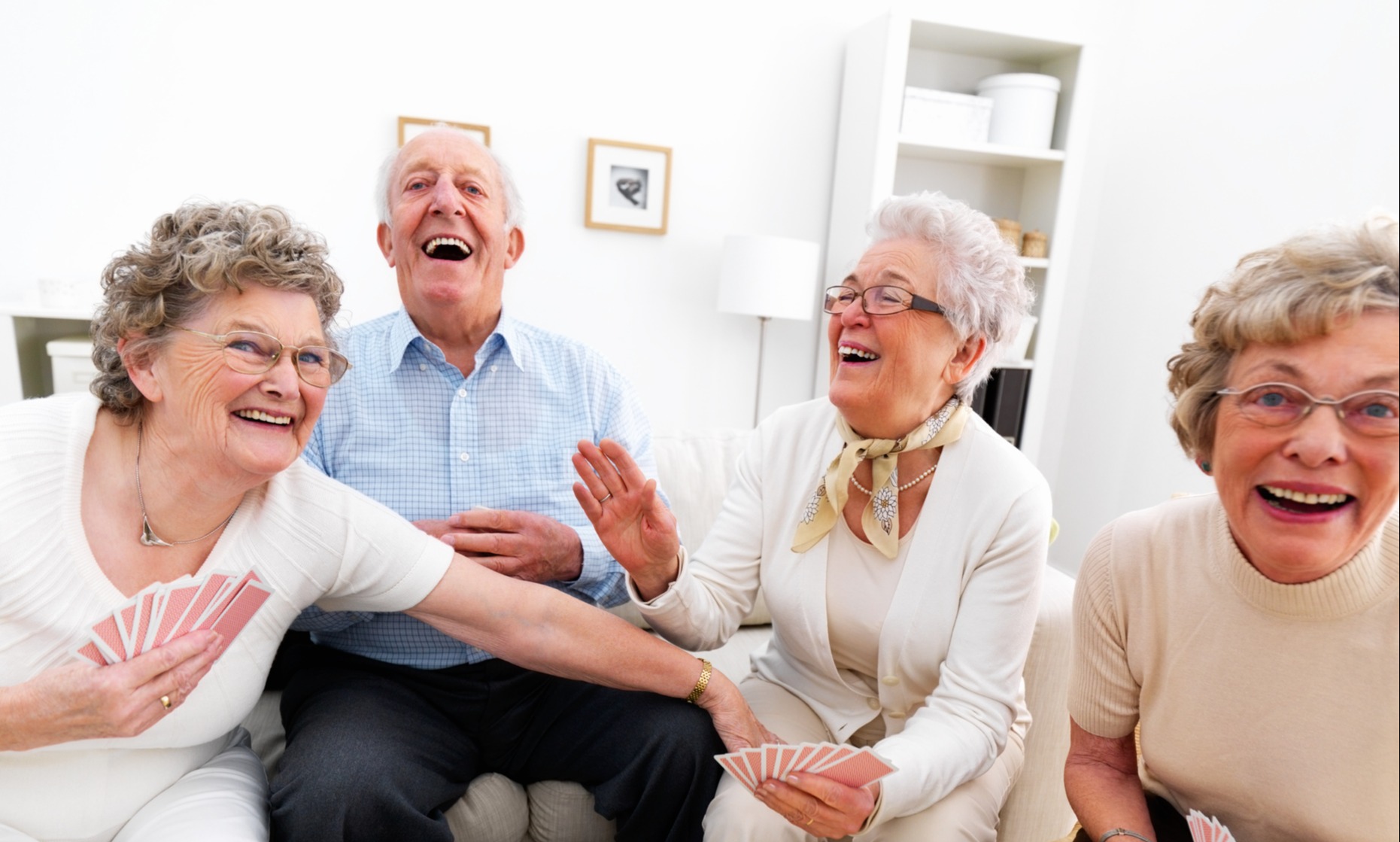 Happy senior man and three women laughing and playing cards at a table