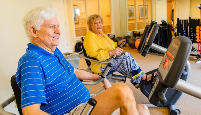 Two senior residents exercising on exercise bikes in a community gym 