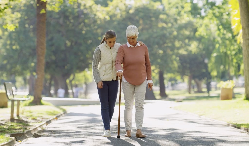senior woman walking with cane alongside caretaker