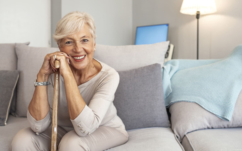 senior holding walking stick smiling while sitting on couch