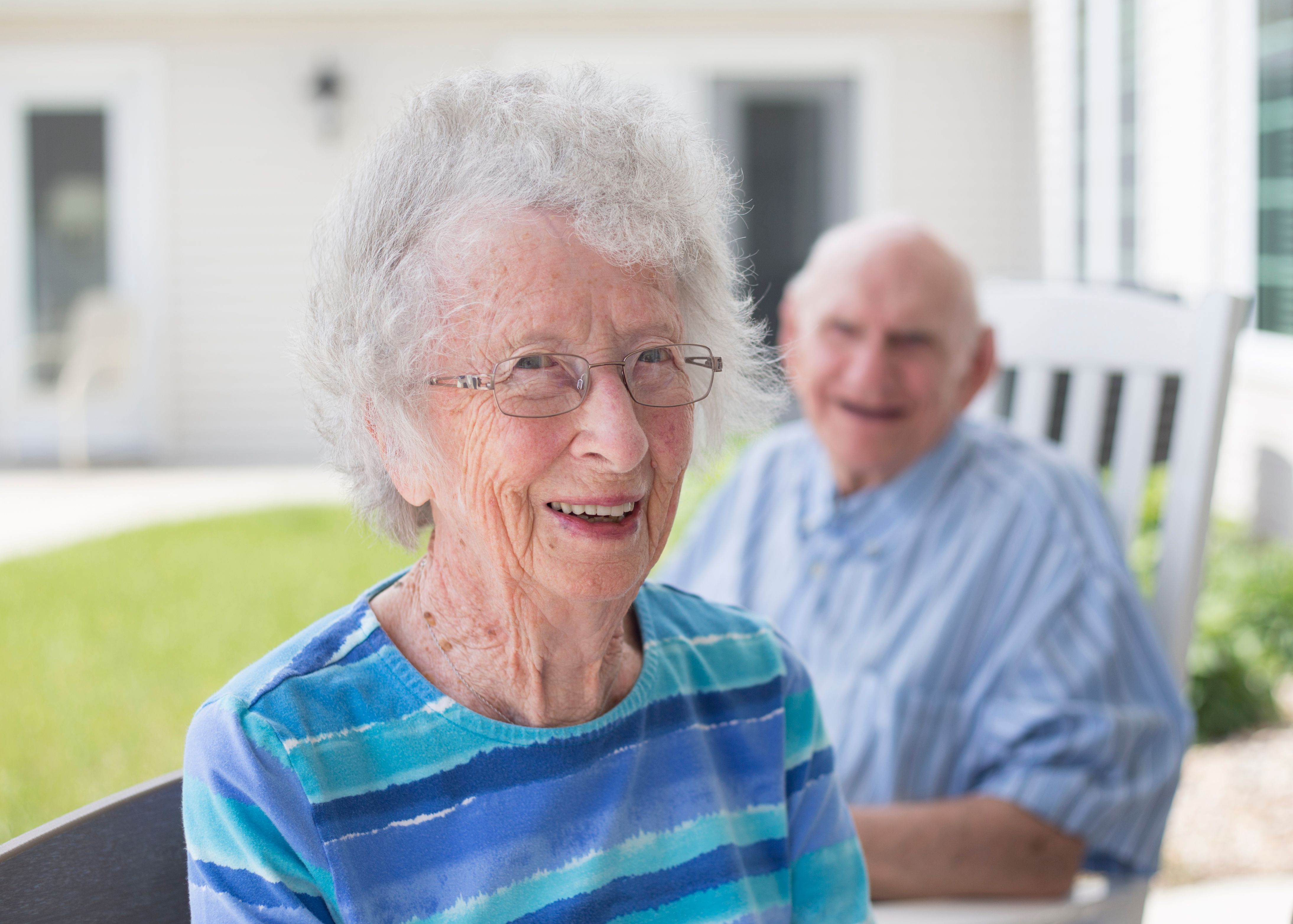 Two seniors sitting outdoors at an assisted living community, smiling at the camera